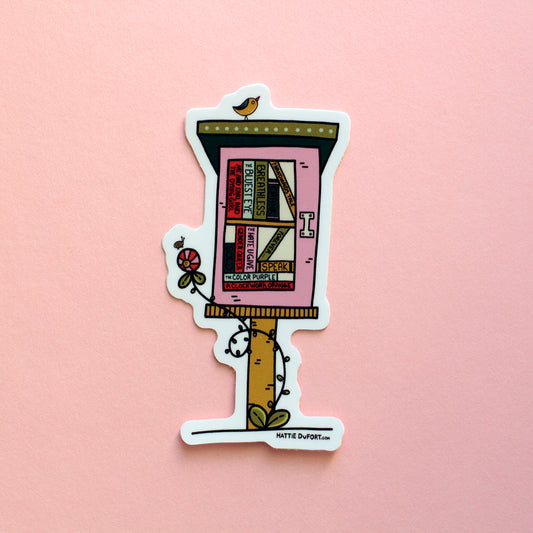 A die-cut sticker featuring a whimsical illustration of a pink little free library with books, a small bird, a flower, and a bee shown on a solid pink background. The brand name Hattie DuFort is printed at the bottom right of the sticker.
